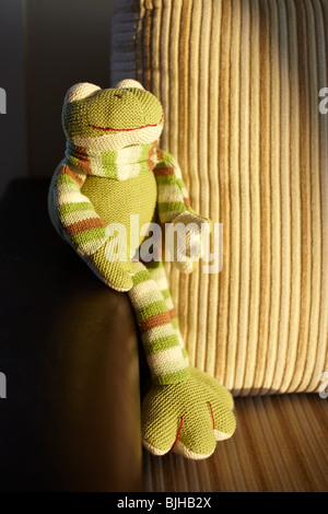 La main verte grenouille jouet tricotés assis dans le dernier rayon de soleil sur un canapé en cuir et velours côtelé marron. Banque D'Images