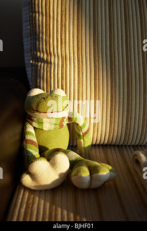 La main verte grenouille jouet tricotés assis dans le dernier rayon de soleil sur un canapé en cuir et velours côtelé marron. Banque D'Images