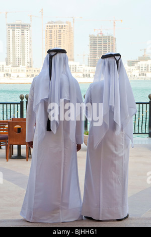 Deux hommes arabes anonyme dans l'habillement blanc traditionnel à la recherche à la construction de nouveaux gratte-ciel modernes sur l'horizon. Banque D'Images