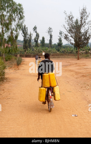 Cycliste portant de lourdes les contenants d'eau le long de la rue. Le Rwanda Banque D'Images