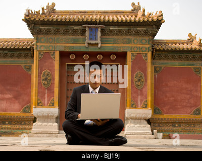 Businessman sitting cross legged outdoors with laptop Banque D'Images