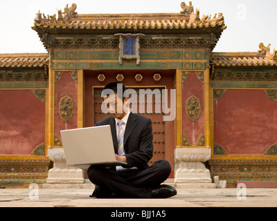 Businessman sitting cross legged outdoors with laptop Banque D'Images