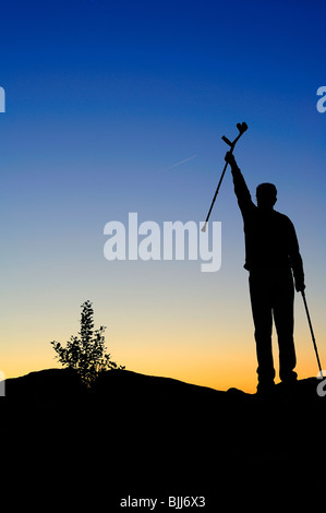 Un homme handicapé se dresse sur une crête, saluant le lever du soleil. Traînée de jet qui passe dans le ciel (peut être clonée si nécessaire). Banque D'Images