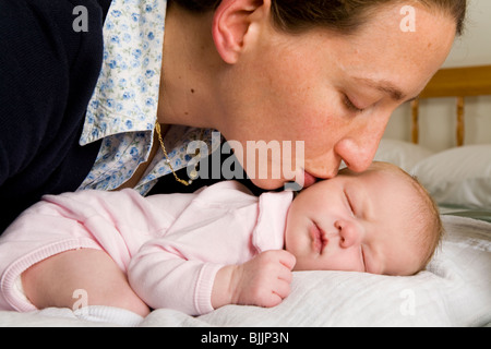 Mère embrassant / baisers dormir / sommeil bébé nouveau-né, sur le lit / lit bébé. Banque D'Images