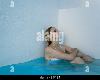 Woman leaning against wall in pool assis et souriant Banque D'Images