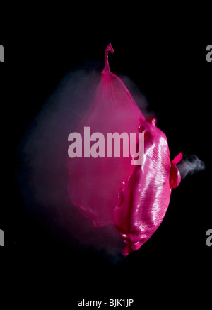 Un ballon rouge rempli de fumée lors de l'éclatement tourné avec une carabine à air. Visible de l'onde sonore Banque D'Images