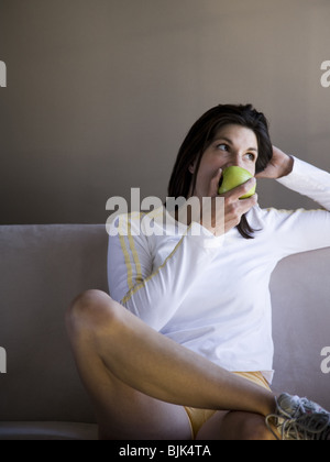 Woman sitting on sofa eating green apple Banque D'Images