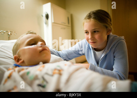 Jeune fille assise par brother in hospital bed Banque D'Images