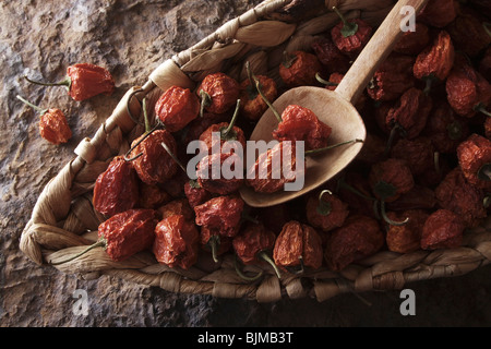 Mini-Peppers (Capsicum) avec une cuillère en bois dans un panier en osier sur une surface en pierre Banque D'Images