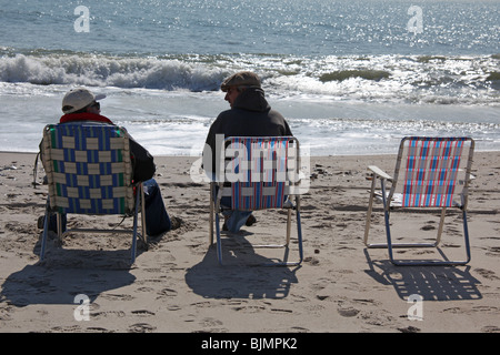 Deux hommes assis sur des chaises sur la plage à Fire Island, New York, sur un hiver doux jour de mars. © Katharine Andriotis Banque D'Images