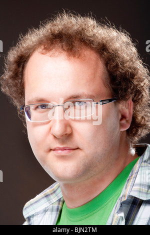 Portrait d'un jeune homme avec des cheveux bouclés et lunettes - isolé sur fond sombre Banque D'Images