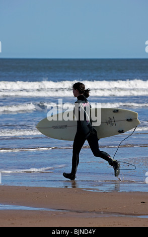 Une femme courir vers les vagues surfer sur une journée ensoleillée, Belhaven Bay Beach, East Lothian, Scotland, UK, Europe Banque D'Images