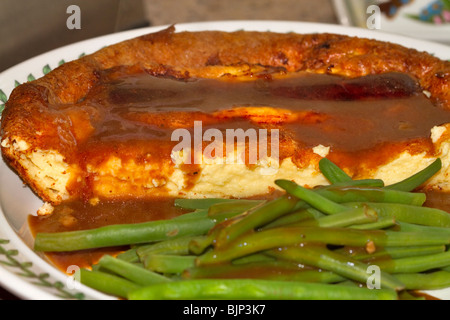 Toad dans le trou, la traditionnelle assiette de saucisses et de yorkshire pudding avec de la sauce et de haricots verts Banque D'Images