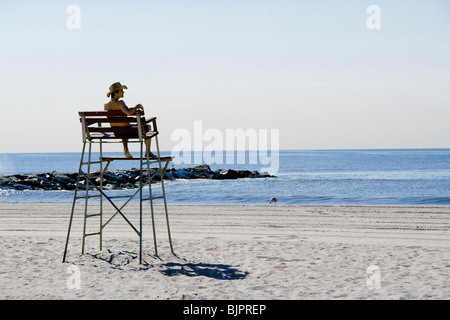 Homme assis dans la chaise de sauveteur à la plage Banque D'Images