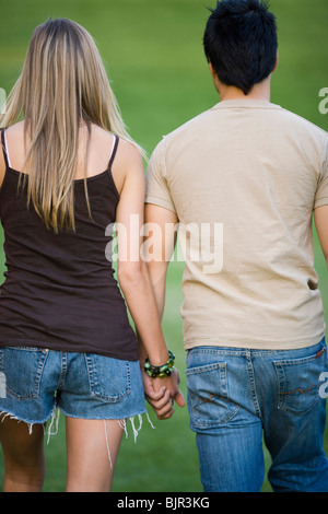 Jeune couple en train de marcher sur une pelouse, bras dessus bras dessous Banque D'Images