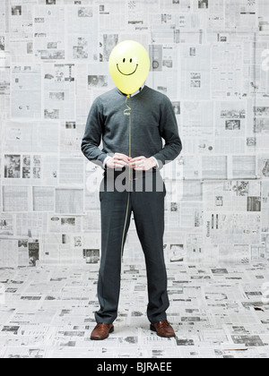 Jeune homme couvrant le visage avec ballon smiley en chambre journaux Banque D'Images