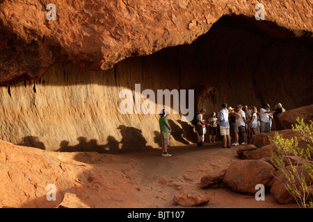 Les touristes dans une grotte de grès de renommée mondiale, l'Uluru ou Ayers Rock , Territoire du Nord, Australie Banque D'Images