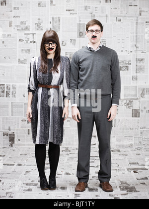 Deux jeunes gens avec fake moustache debout dans journaux couverts chambre, studio shot Banque D'Images