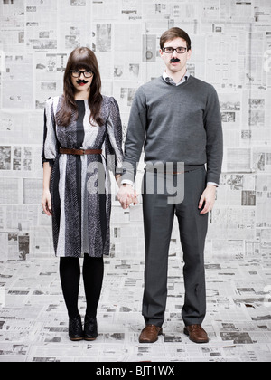 Deux jeunes gens avec fake moustache debout dans journaux couverts chambre, studio shot Banque D'Images