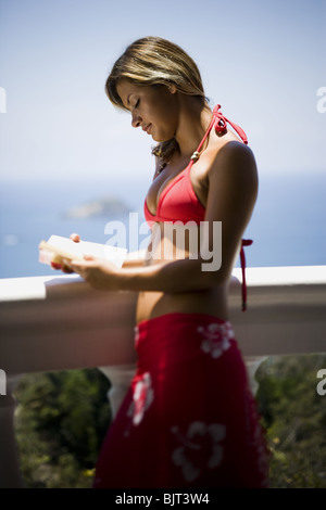Femme lisant et penchées sur un balcon donnant sur l'océan Banque D'Images