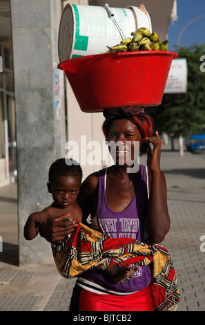 Portrait d'une jeune mère street vendeur porter un bébé et un seau sur la tête. La ville de Benguela, en Angola. L'Afrique. Banque D'Images