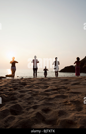 Les femmes pratiquant le yoga sur la plage au coucher du soleil Banque D'Images