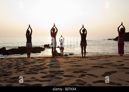 Les femmes pratiquant le yoga sur la plage au coucher du soleil Banque D'Images