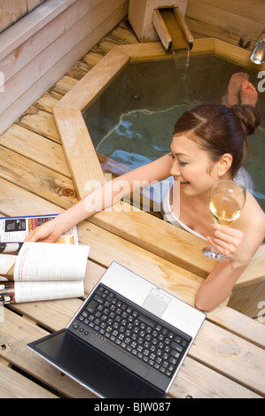 Femme à l'aide de son ordinateur portable et boire du vin dans un bain à remous Banque D'Images