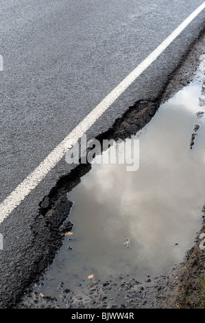 Trou de pot rempli de pluie sur le côté de la route avec cassé tarmac et ligne blanche Banque D'Images