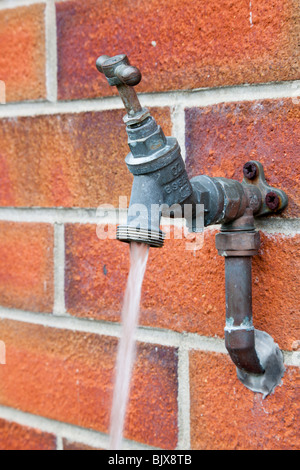 L'eau courante découlant d'un robinet extérieur allumé et fixe à un mur de briques Banque D'Images