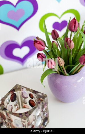 Un vase de tulipes violet en face de papier peint couleur décoré d'un motif coeur Banque D'Images