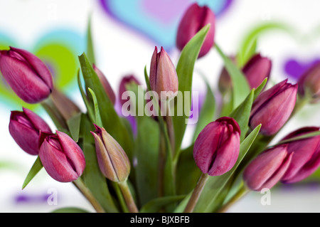 Un vase de tulipes violet en face de papier peint couleur décoré d'un motif coeur Banque D'Images