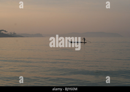 Bateau de pêche qui se profile par la brume du matin du soleil, des palmiers à l'horizon Banque D'Images