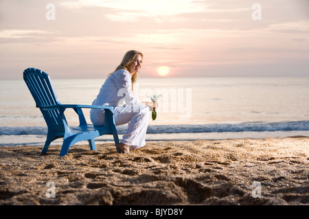 Woman sitting on chair on beach pendant au coucher du soleil Banque D'Images