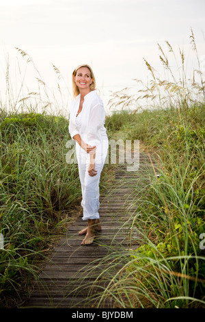 Femme en blanc se promener en plein air au milieu des herbes de la plage Banque D'Images