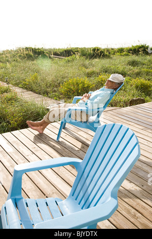 Senior man sitting on chair sieste au soleil sur la terrasse en bois Banque D'Images