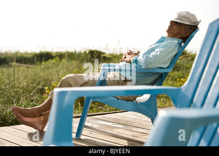 Senior man sitting on chair sieste au soleil sur la terrasse en bois Banque D'Images