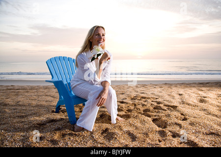 Woman sitting on chair on beach pendant au coucher du soleil Banque D'Images