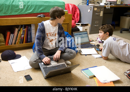 Les adolescents dans la chambre avec un ordinateur portable et les manuels scolaires, l'écoute de l'iPod et lecteurs MP3 avec des écouteurs, et envoyant les amis Banque D'Images