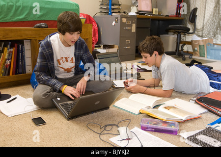 Les adolescents dans la chambre avec un ordinateur portable et les manuels scolaires, l'écoute de l'iPod et lecteurs MP3 avec des écouteurs, et envoyant les amis Banque D'Images