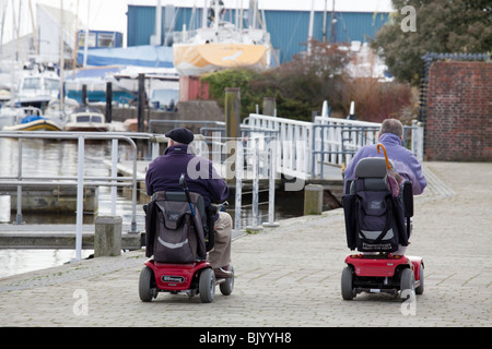 Deux hommes en fauteuil roulant motorisé sur le quai à Lymington. Banque D'Images