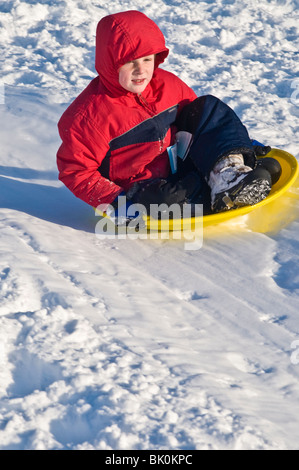 Les jeunes enfants des familles sur des traîneaux snowy city park hillside. Banque D'Images