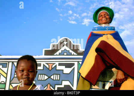 Ndebele personnes portant le costume traditionnel en face d'une maison peinte traditionnellement, l'Afrique du Sud. Banque D'Images