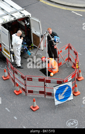 Téléphone BT ingénieurs travaillant dans la rue et l'accès aux câbles souterrains via open manhole Banque D'Images