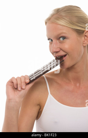 Jolie jeune femme de race blanche de manger une barre de chocolat et regardant la caméra Banque D'Images