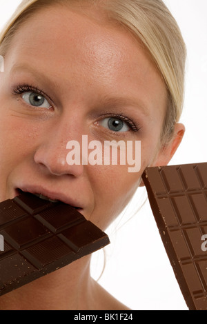 Jolie jeune femme de race blanche de manger une barre de chocolat et regardant la caméra Banque D'Images