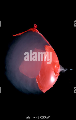 Un ballon rouge rempli de fumée lors de l'éclatement tourné avec une carabine à air. Visible de l'onde sonore et le culot de sortir. Banque D'Images