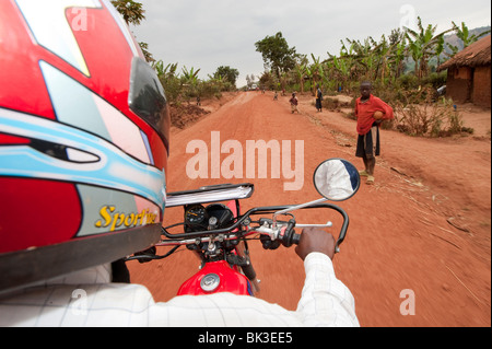 En descendant la rue du village de poussière au Rwanda sur un cycle moteur Banque D'Images