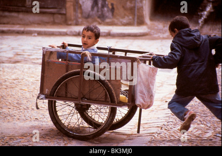 Scène urbaine de rue d'enfants jouant avec un chariot à deux roues au Maroc, en Afrique du Nord Banque D'Images