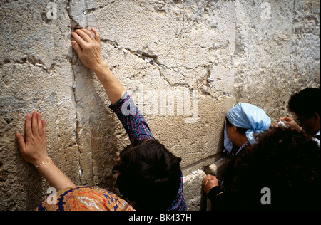 Les femmes priant et en plaçant des prières écrites sur du papier dans les fissures du Mur occidental, à Jérusalem, Israël Banque D'Images